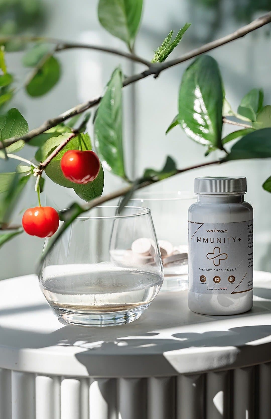 Branche d'acérola, verre d'eau et flacon Immunity+